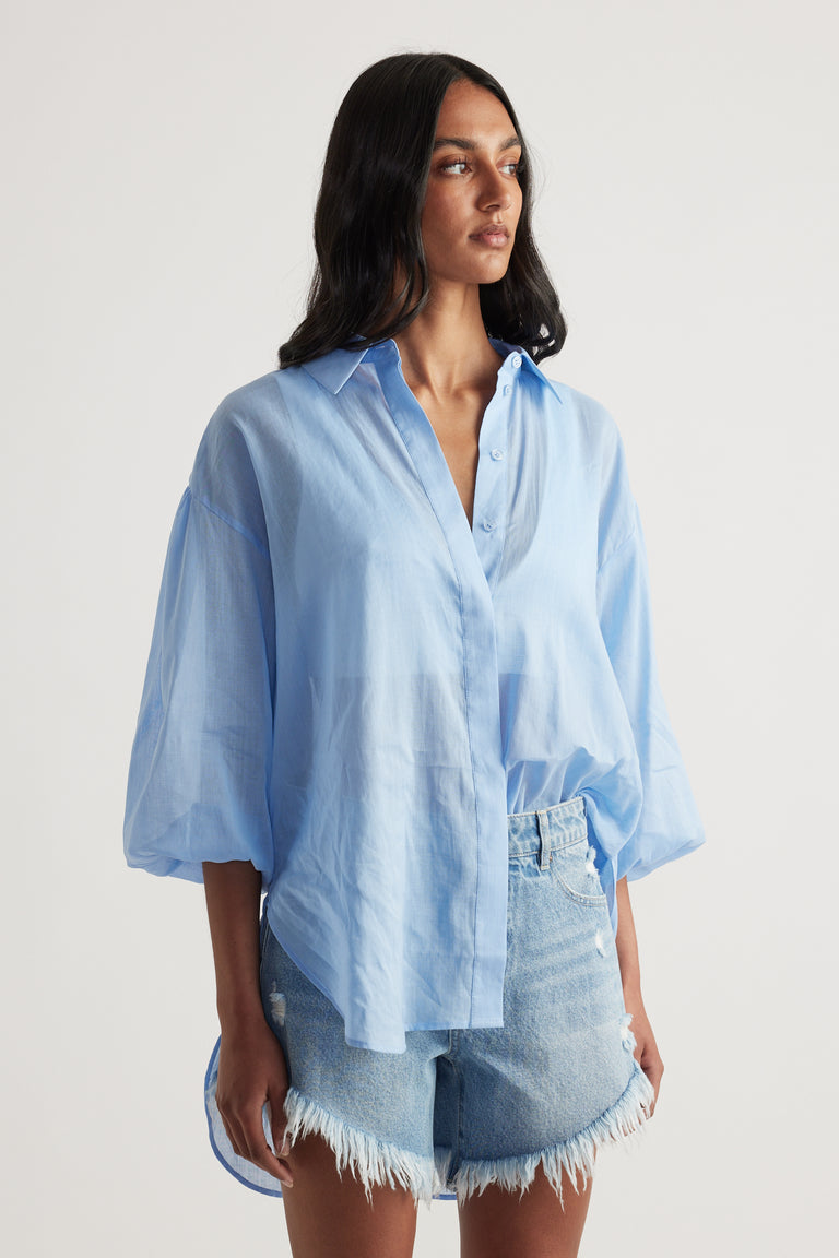 Woman wearing a light blue oversized collared shirt with frayed denim shorts