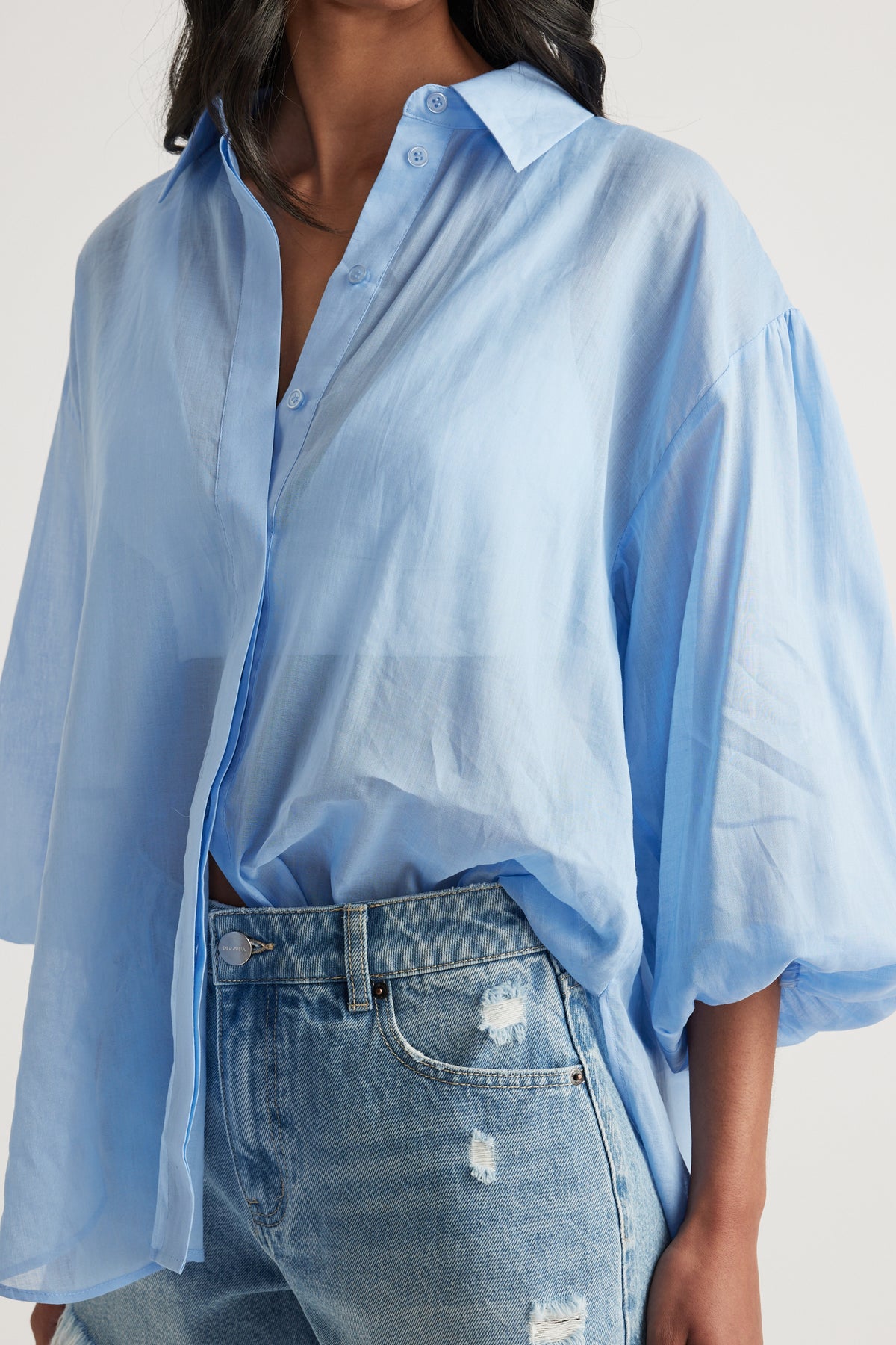 Woman wearing a light blue oversized button through shirt with distressed blue jeans