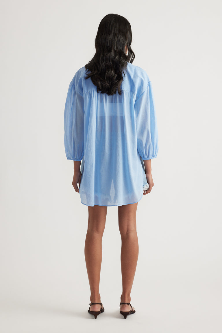 Back view of a woman wearing a light blue oversized collared shirt with long sleeves and black heels