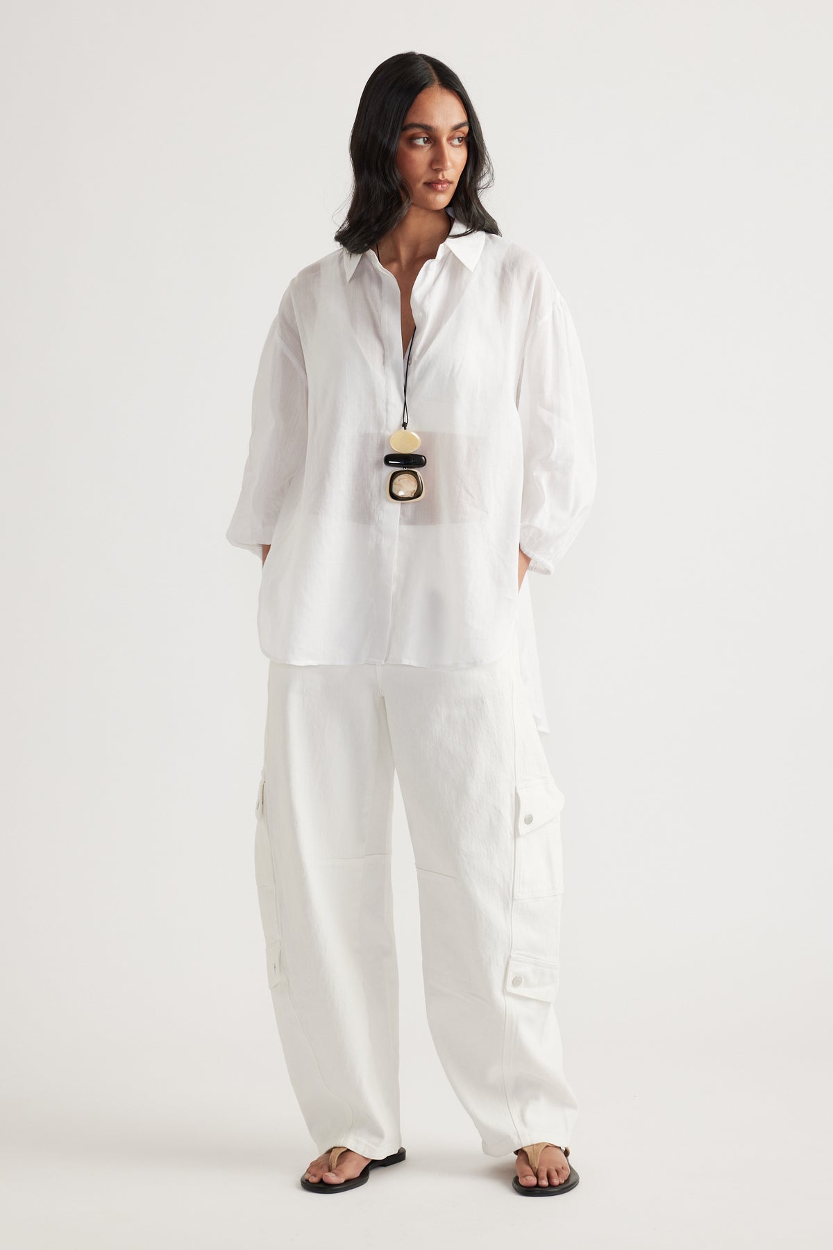 Woman wearing a white oversized collared shirt with white cargo pants and black sandals