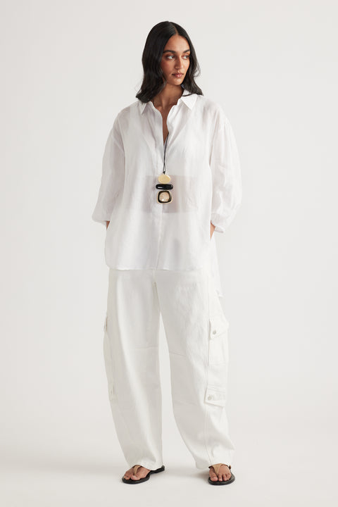 Woman wearing a white oversized collared shirt with white cargo pants and black sandals