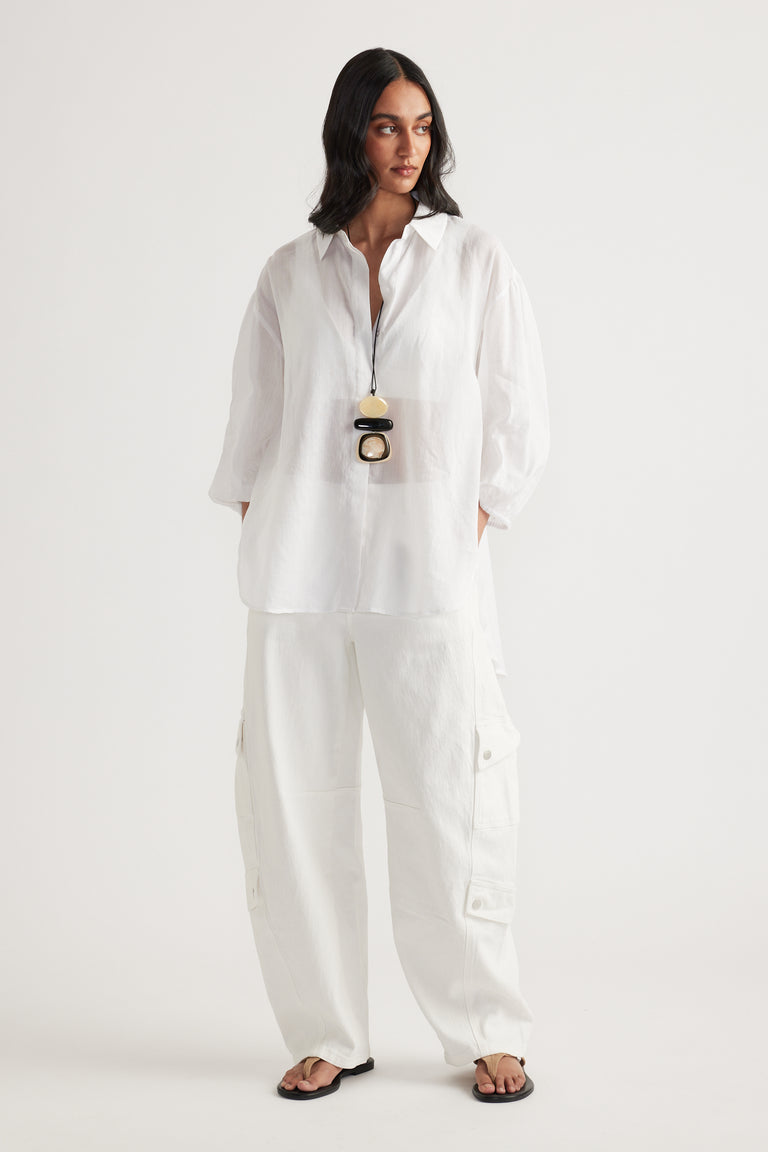 Woman wearing a white oversized collared shirt with white cargo pants and black sandals