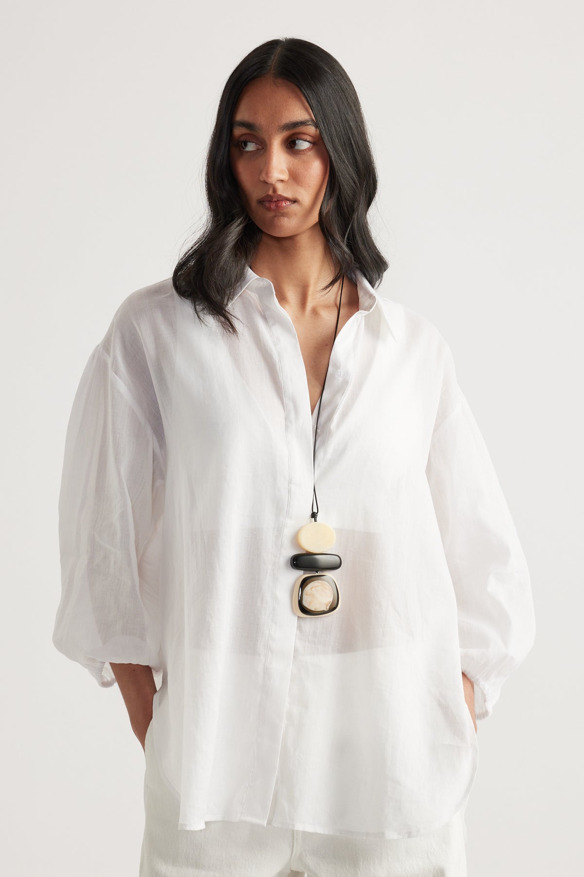 Woman wearing an oversized white button front shirt with relaxed sleeves and a statement pendant necklace