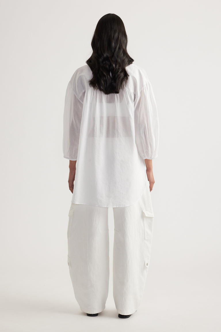 Back view of a woman in a white oversized collared shirt with long sleeves, white pants and black shoes