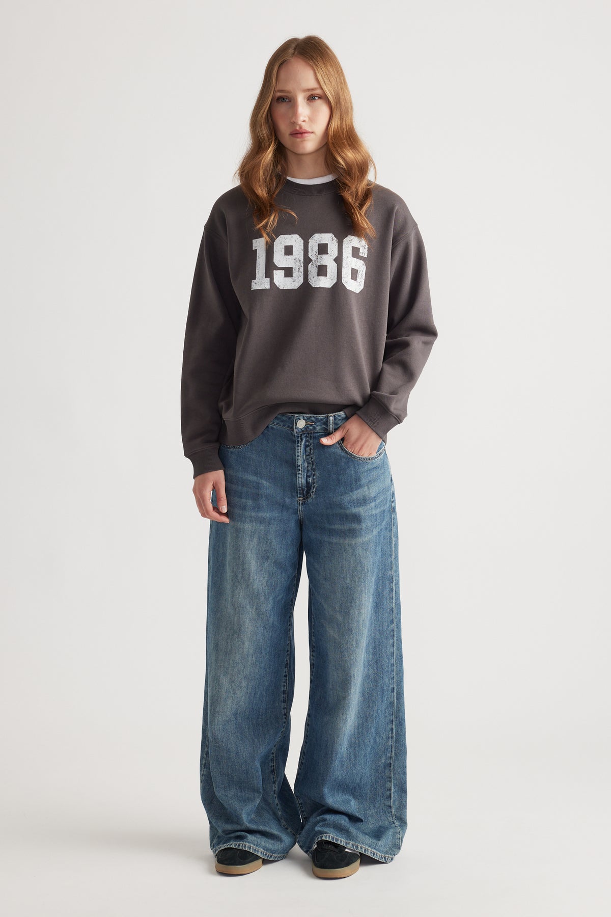 Woman wearing a washed black sweatshirt with bold 1986 print paired with wide-leg blue denim jeans for a laid-back look