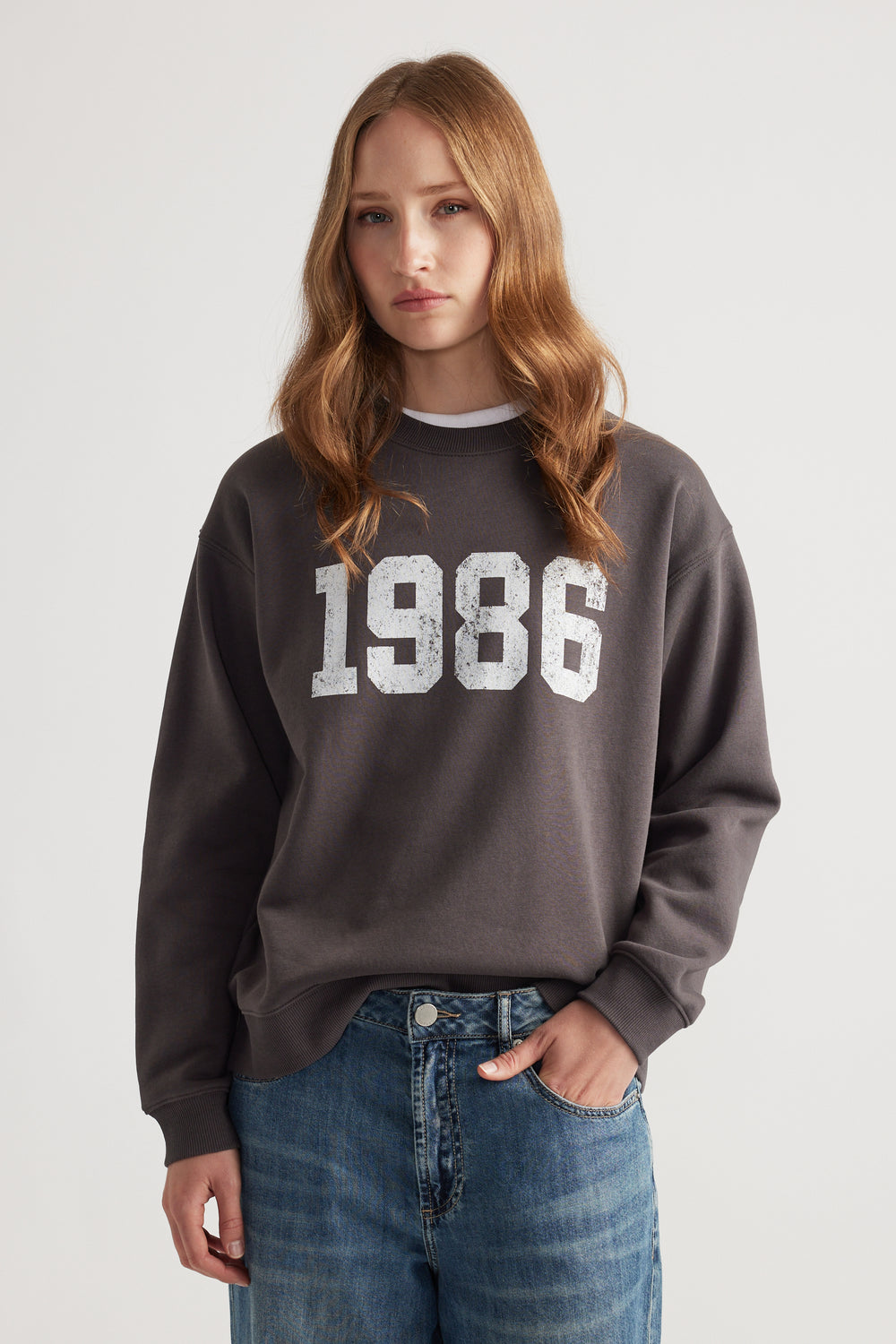Woman wearing a washed black oversized crew neck sweatshirt with a vintage 1986 print paired with relaxed blue denim jeans