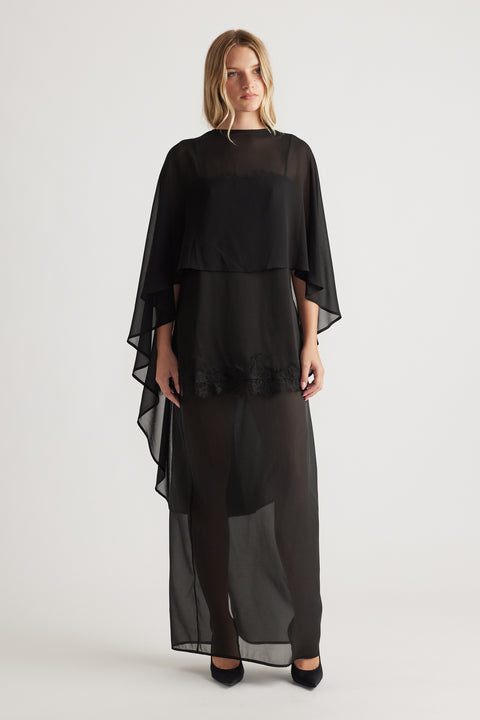 Front view of a black flowing georgette cape top layered over a sheer long skirt with lace detail at hem