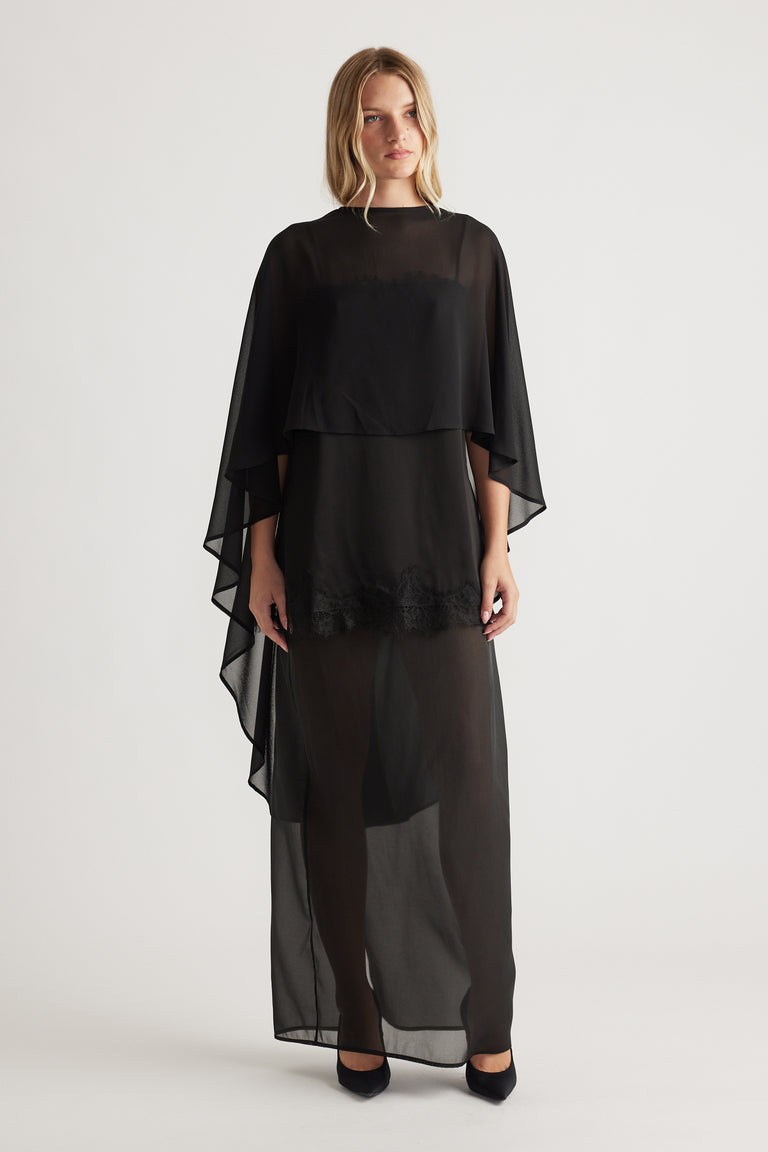 Front view of a black flowing georgette cape top layered over a sheer long skirt with lace detail at hem
