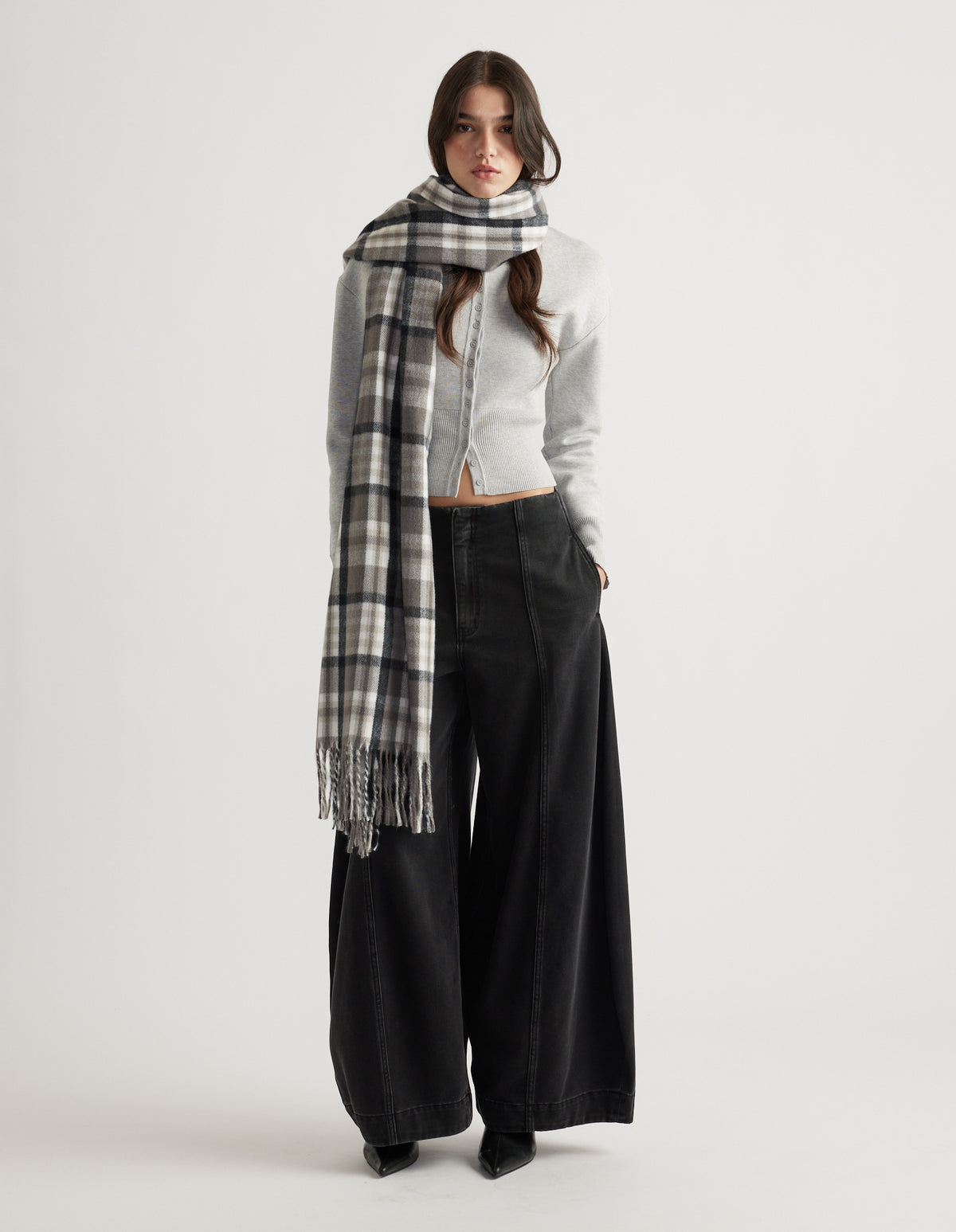 Woman wearing a long checked scarf wrapped loosely around her neck, paired with wide-leg black pants and a fitted grey top