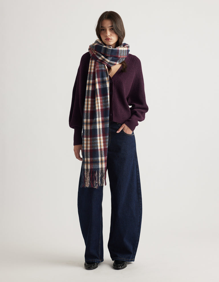 Woman wearing a deep plum knit cardigan paired with wide-leg dark denim jeans and a long navy plaid scarf