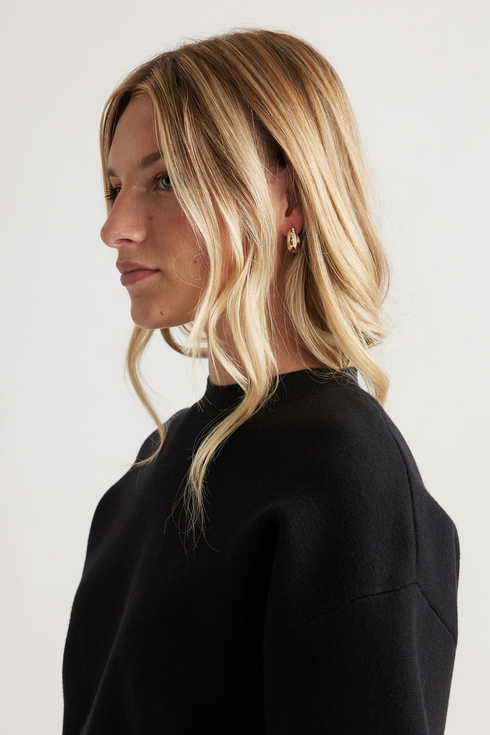 Side profile of woman with blonde waves wearing gold hoop Cat Earring Multi Pack styled with a simple black top for everyday elegance