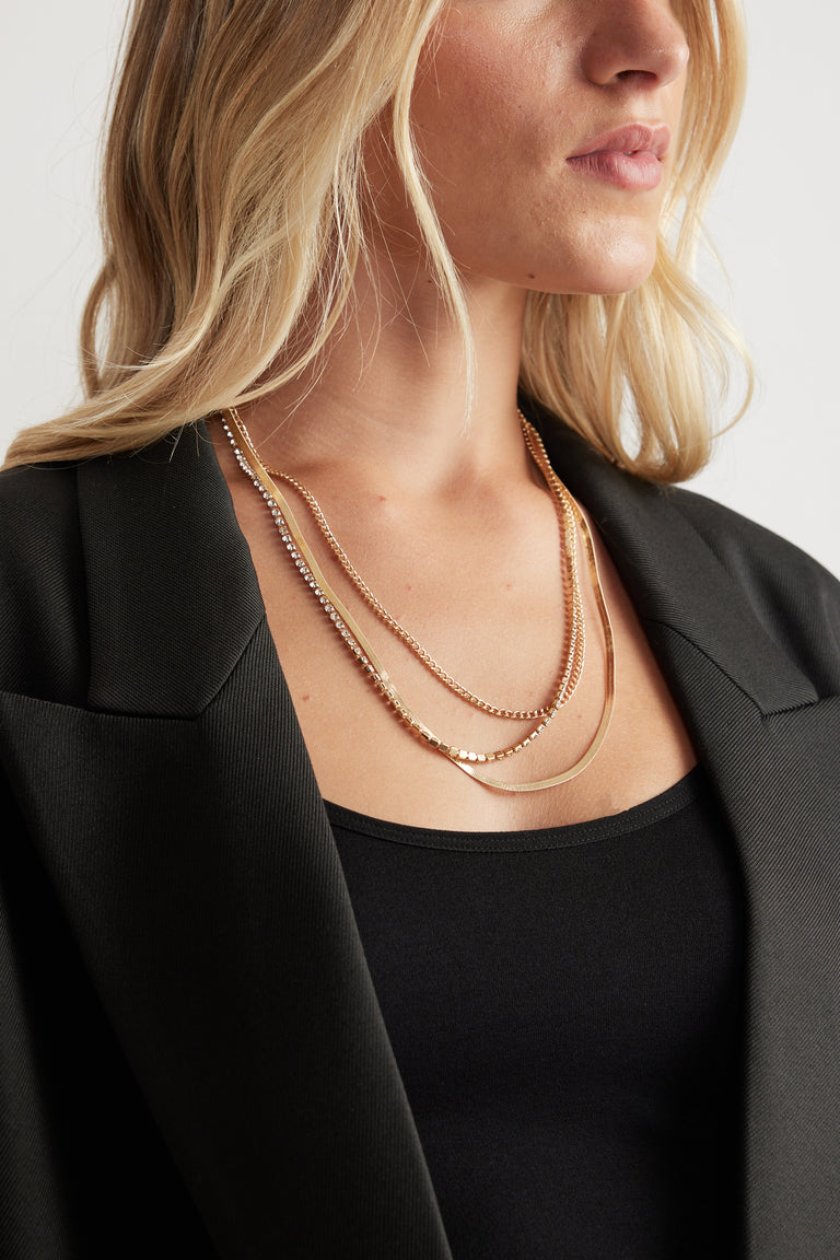 Close-up of a woman wearing the gold-toned Callie Layered Necklace styled with a black top and blazer by DECJUBA.