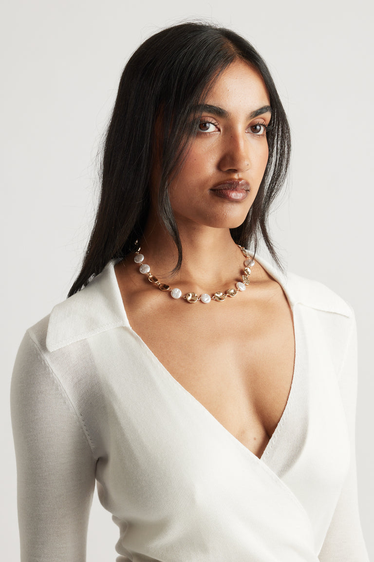 Woman wearing a gold and pearl necklace paired with a deep V-neck white knit top for a refined, elegant style