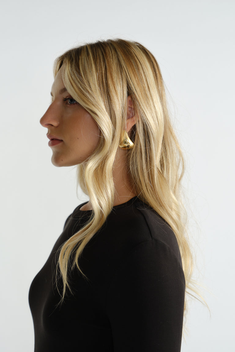 Profile of a woman with long blonde hair wearing sculptural gold statement hoop earrings and a fitted black top