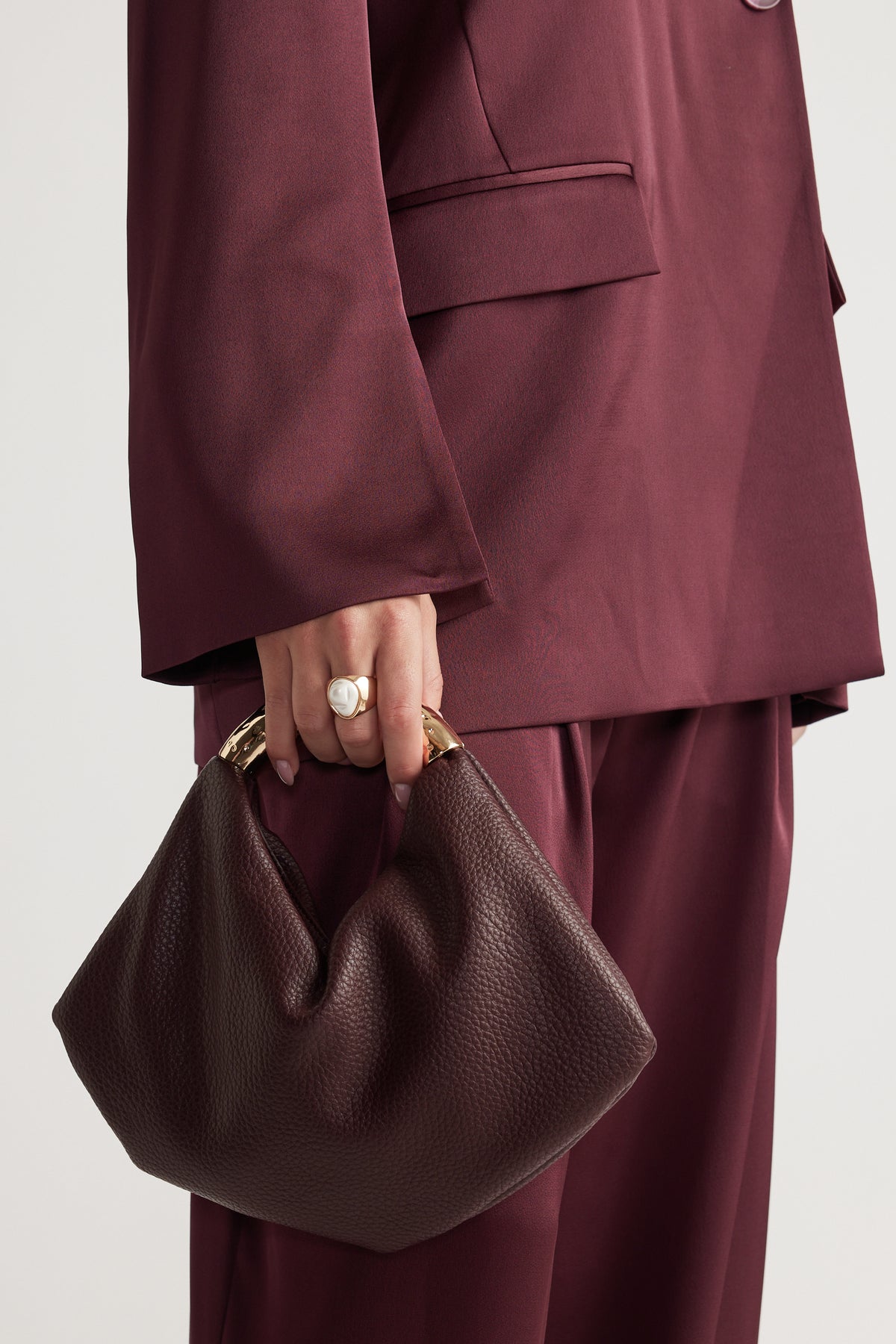 Close-up of hand wearing a gold and white statement ring holding a textured dark brown handbag with gold handles