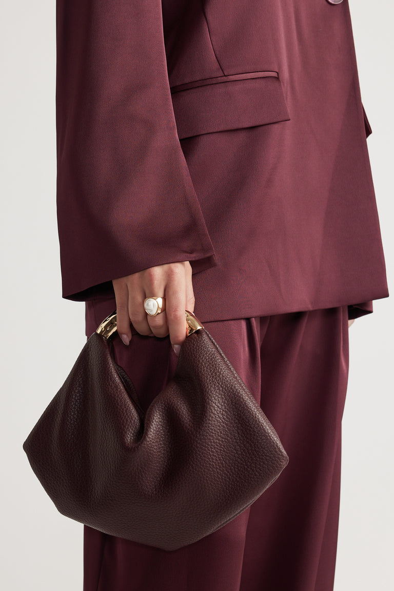 Close-up of hand wearing a gold and white statement ring holding a textured dark brown handbag with gold handles