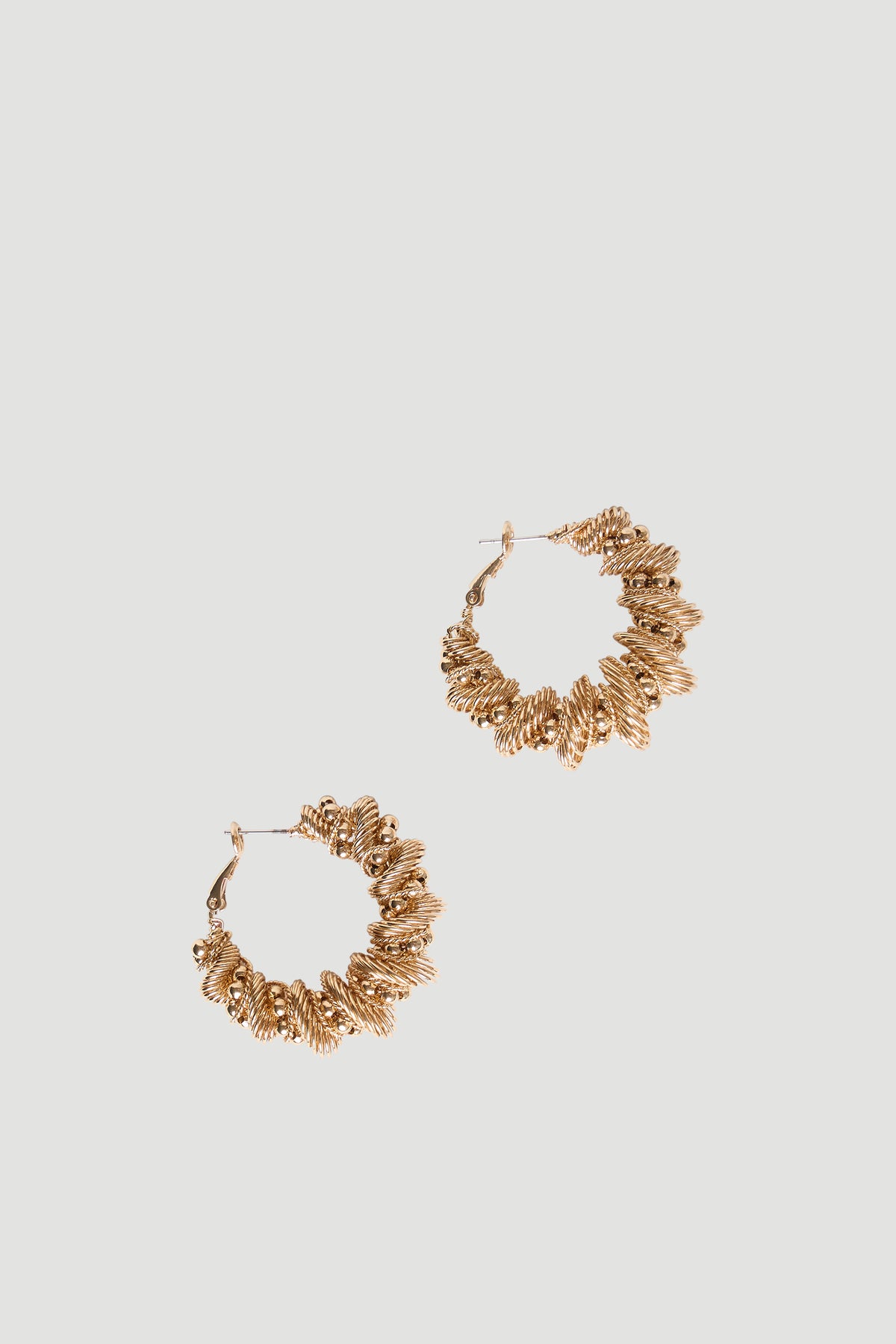 Pair of gold-tone braided twist hoop earrings with mini bead accents and hinged omega back closures on pale background