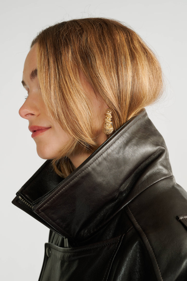 Profile of woman with short blonde hair wearing gold textured earrings and a high-collar black leather jacket