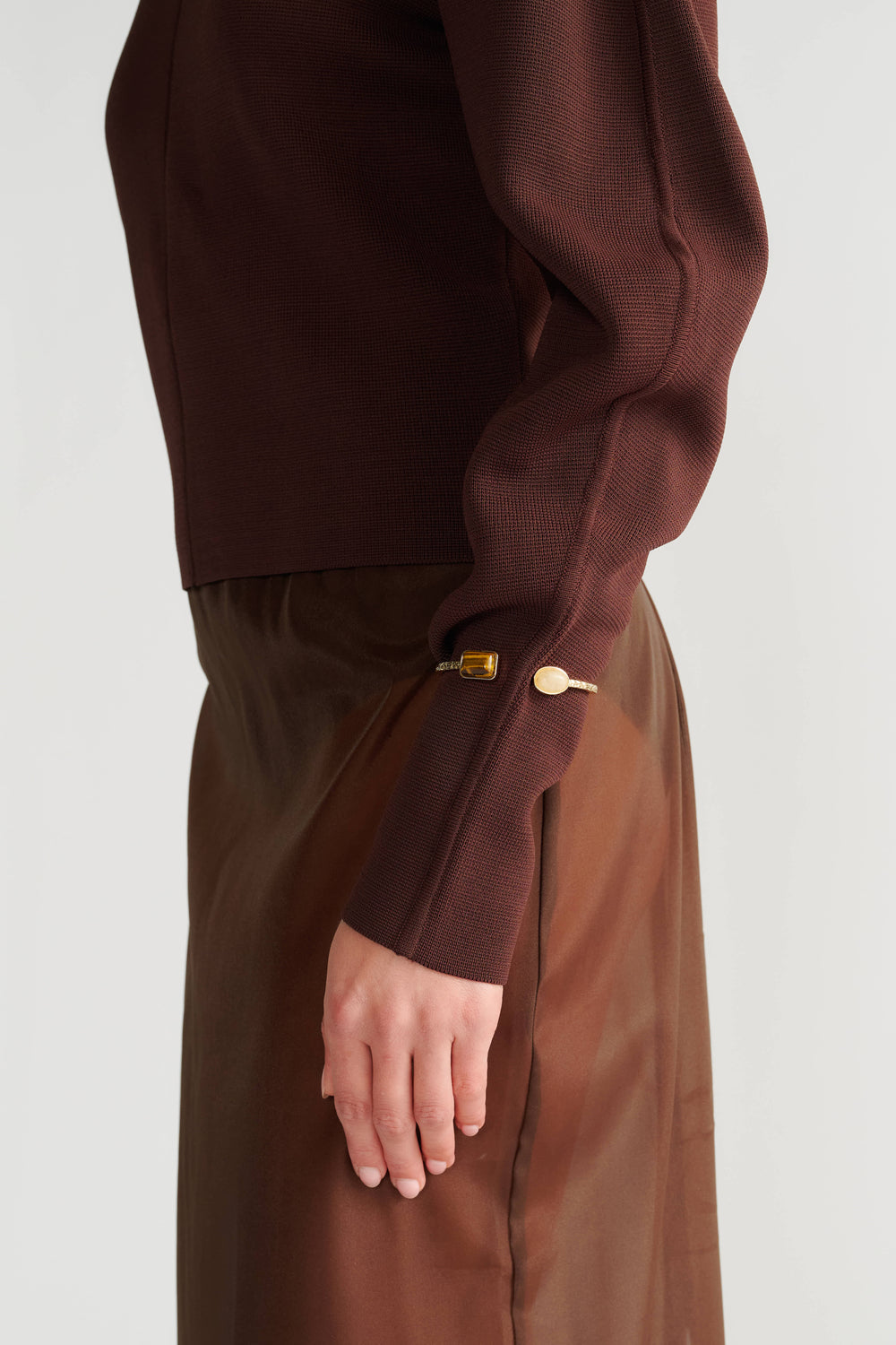 Close-up of a gold-toned stone cuff bracelet worn with a rich brown fitted knit top and matching skirt.