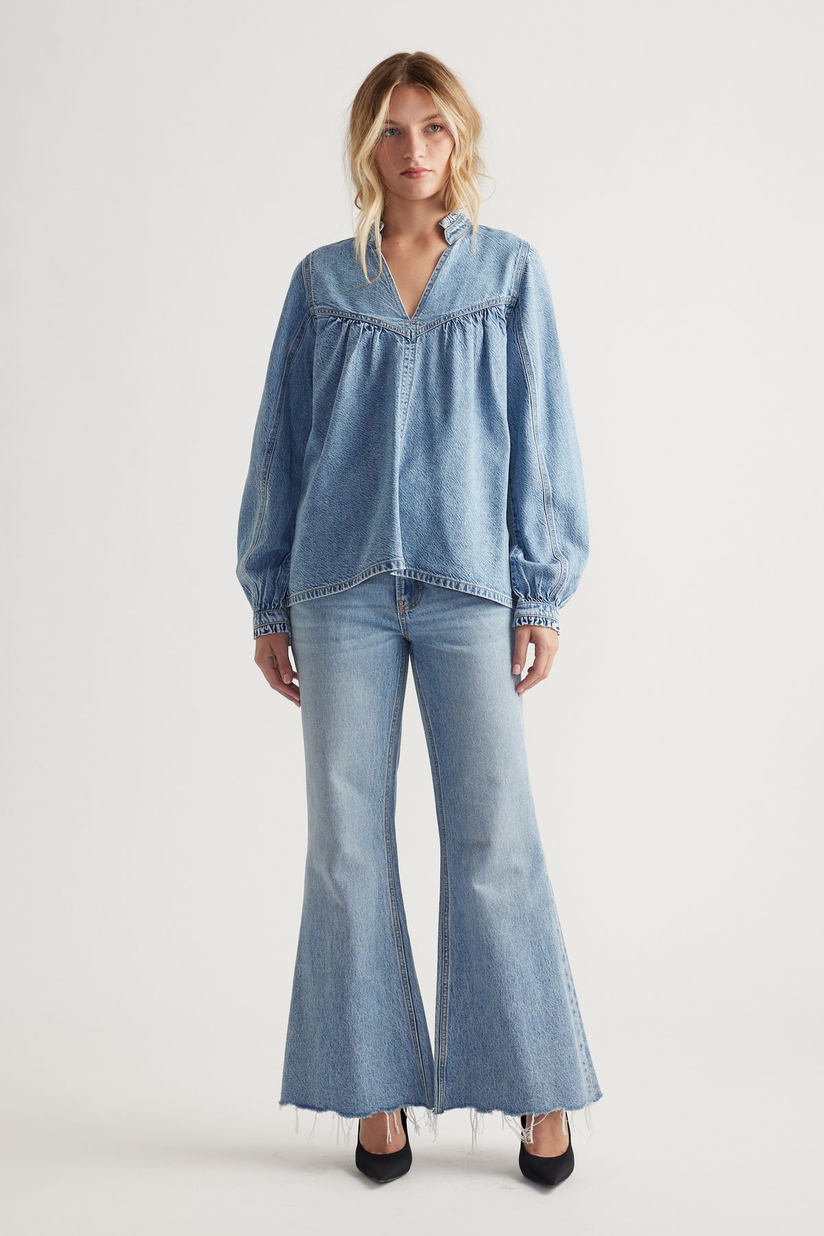 Woman wearing a relaxed fit denim blouse with balloon sleeves paired with light wash flared jeans and black heels
