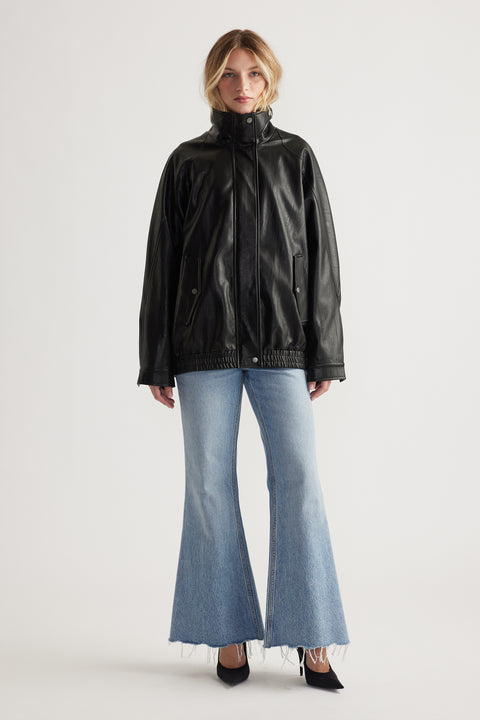 Woman wearing a black high-neck leather jacket paired with light wash high-rise flare jeans and black heels.