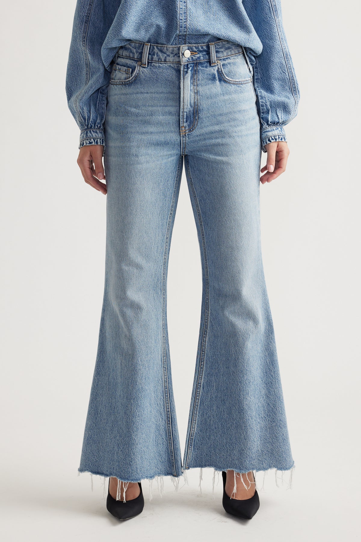 Light wash high-rise flare jeans with raw hem detail paired with a casual denim top and black pointed heels.
