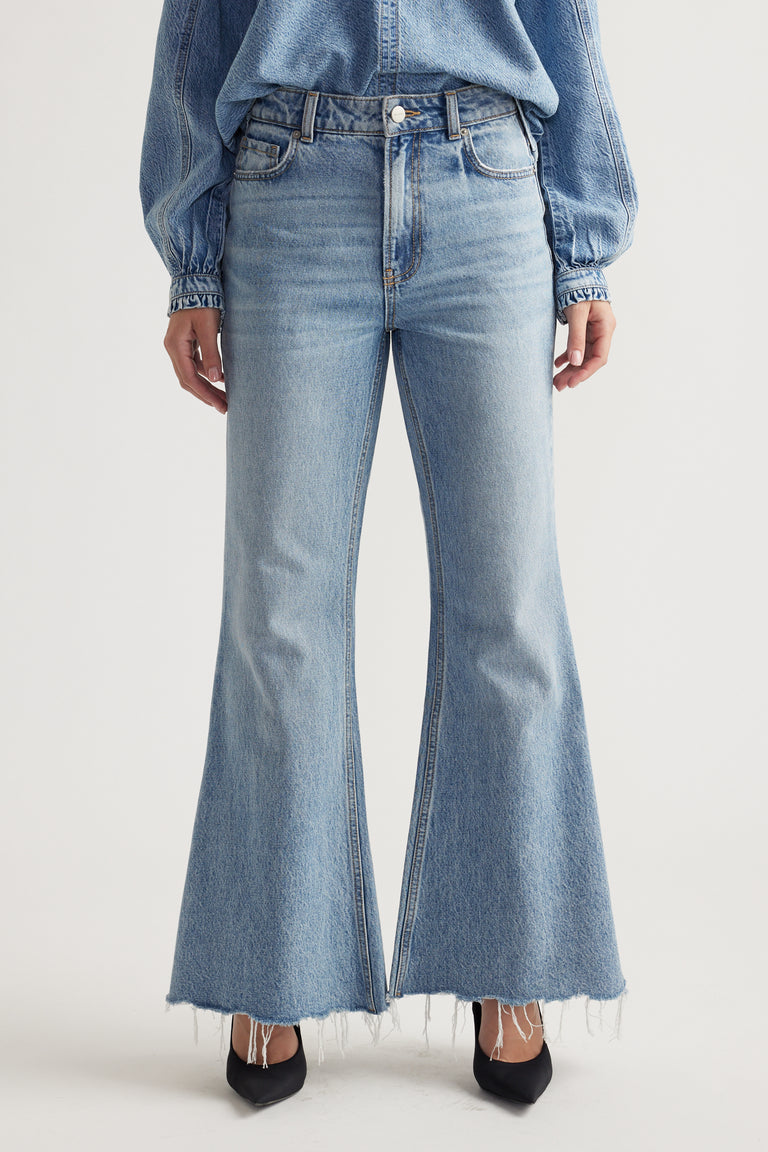 Light wash high-rise flare jeans with raw hem detail paired with a casual denim top and black pointed heels.