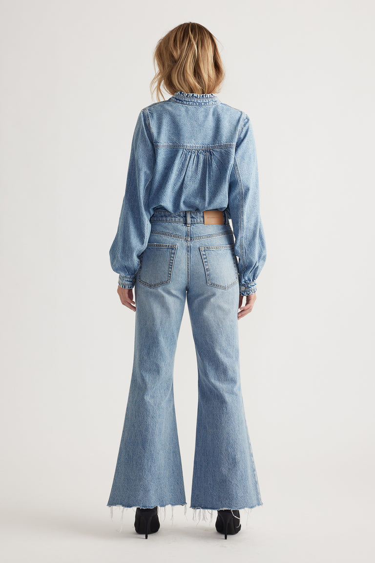 Woman wearing light wash high-rise flare jeans paired with a loose denim shirt and black heels, viewed from behind.