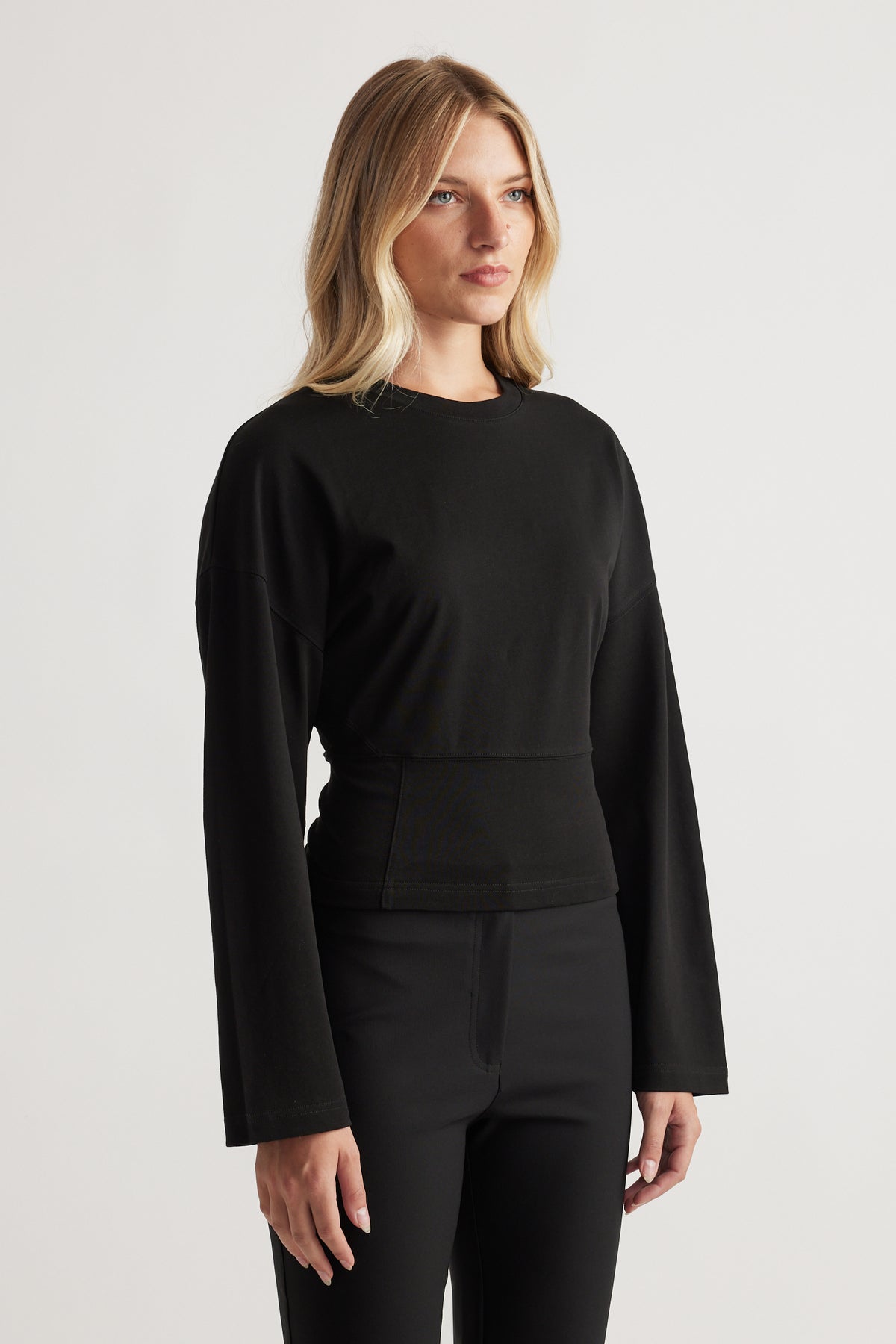 Woman wearing a fitted black long sleeve top with a slightly cinched waist paired with tailored black pants