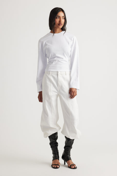 Woman wearing a fitted white long sleeve top paired with wide-leg white pants and black heeled boots