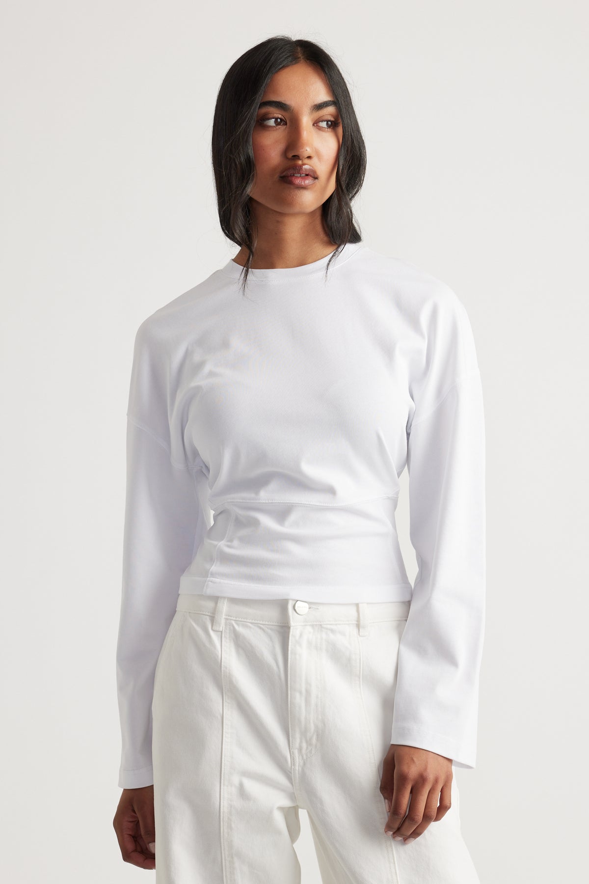 Woman wearing a fitted white long-sleeve top with a high neckline paired with high-waisted white pants