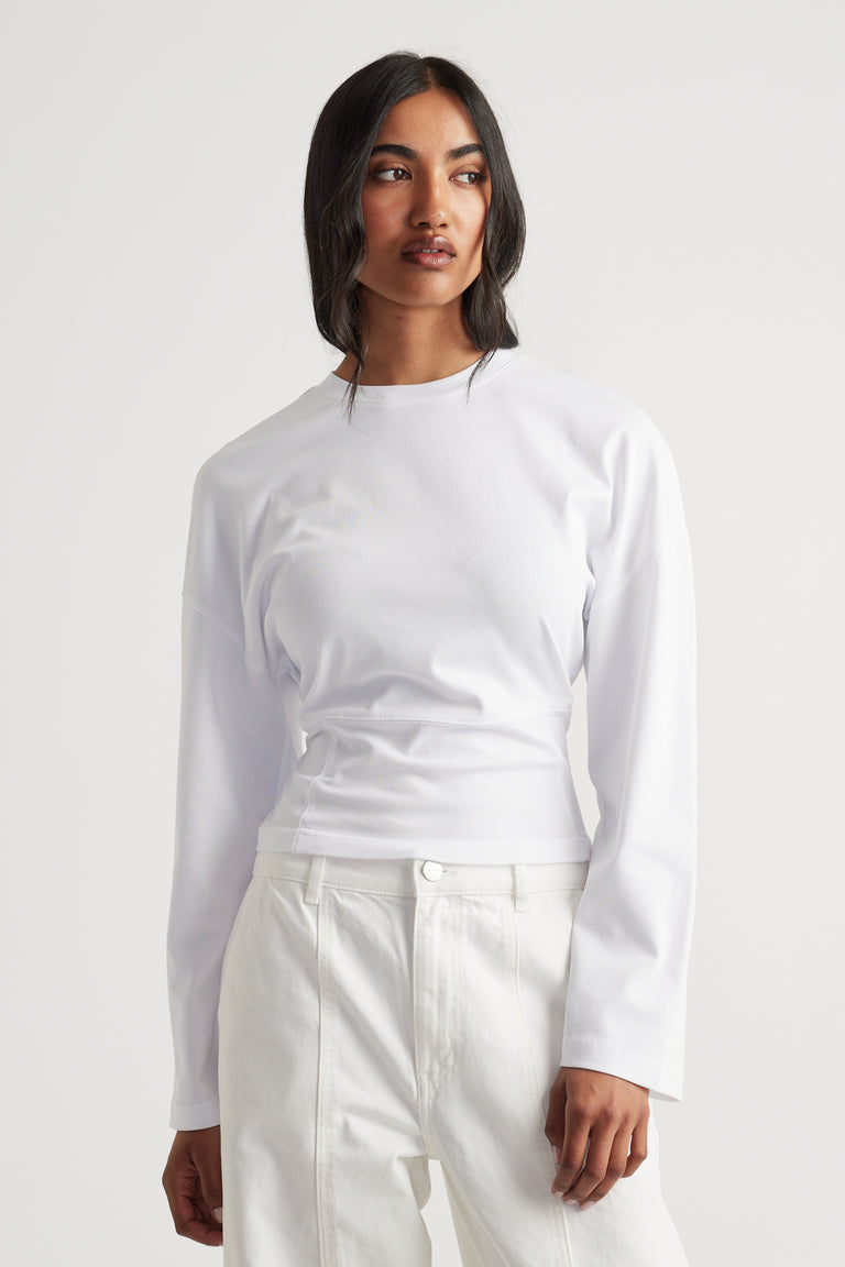 Woman wearing a fitted white long-sleeve top with a high neckline paired with high-waisted white pants