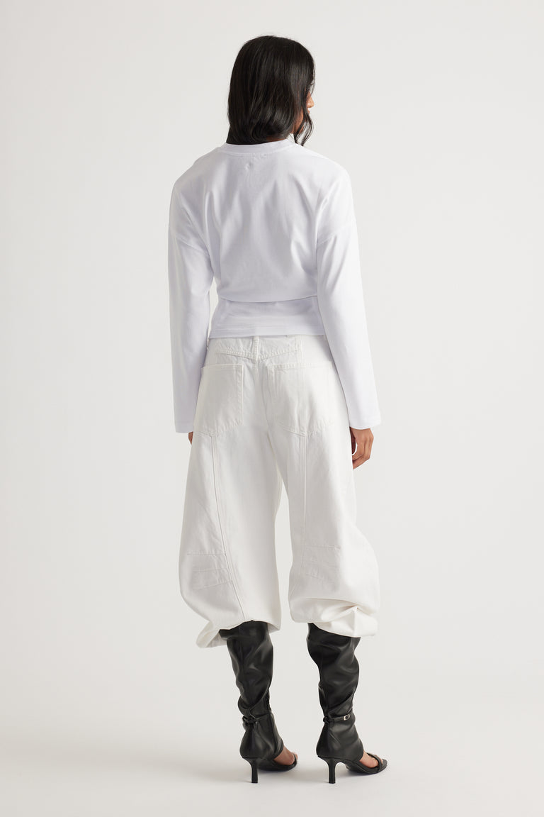 Back view of a sleek white long sleeve top paired with loose white pants and black heeled boots for a chic look