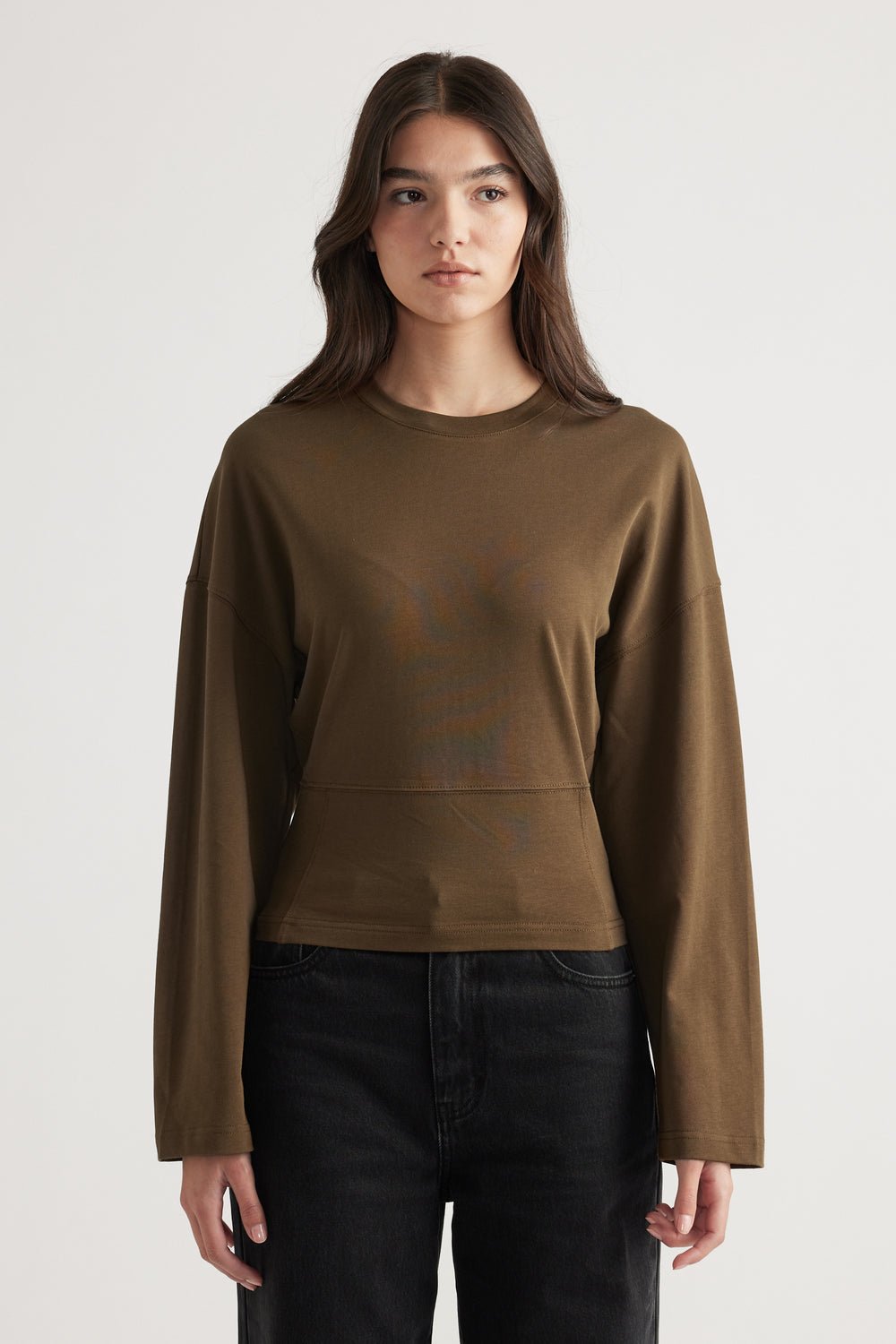Woman wearing an olive green long sleeve top with a relaxed fit paired with high-waisted black jeans.