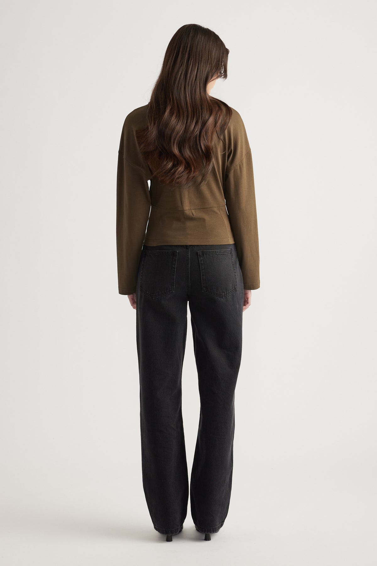 Woman with long wavy hair wearing an olive green long-sleeve top paired with relaxed-fit black jeans