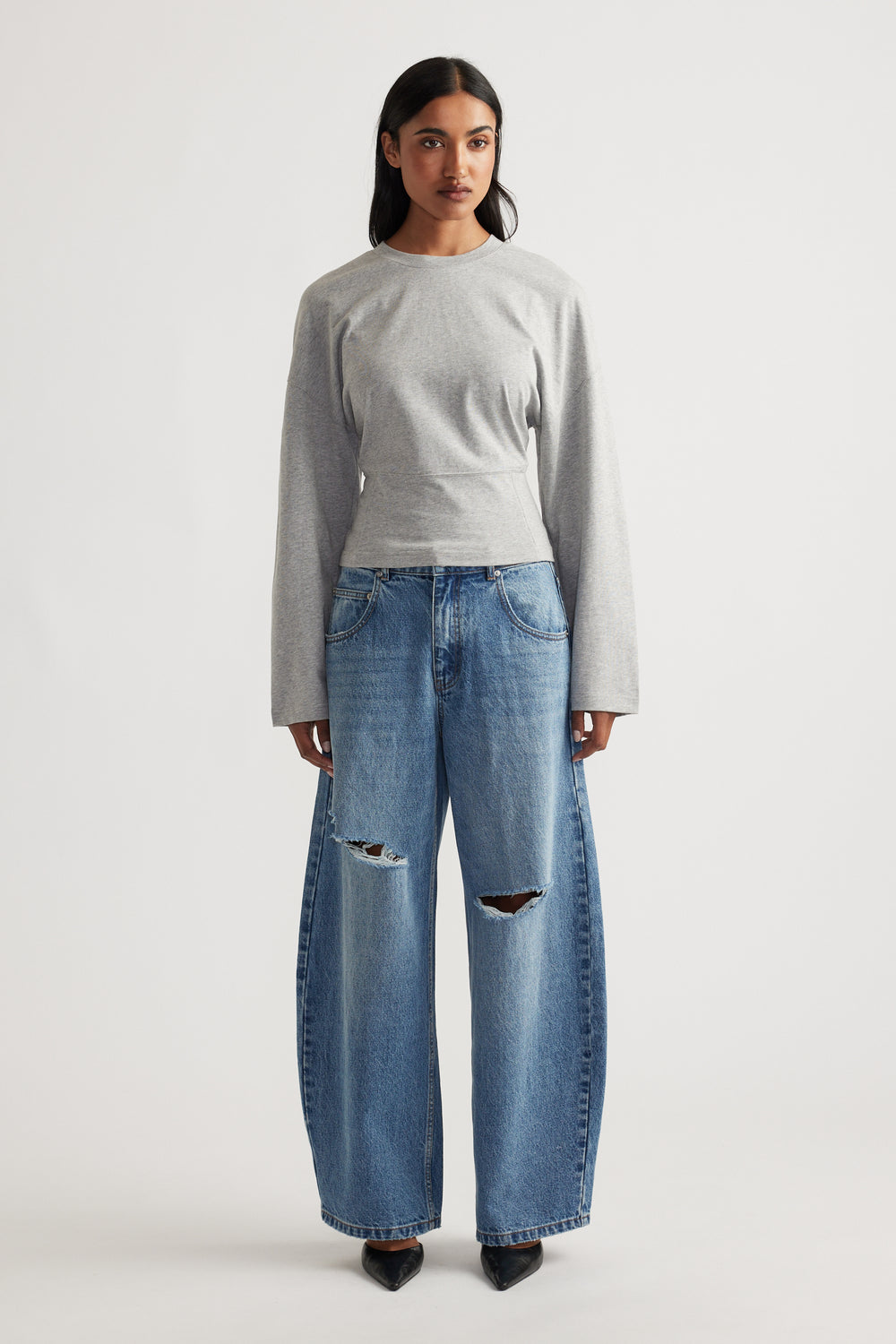 Grey fitted long sleeve top paired with wide-leg distressed blue denim jeans and black pointed shoes