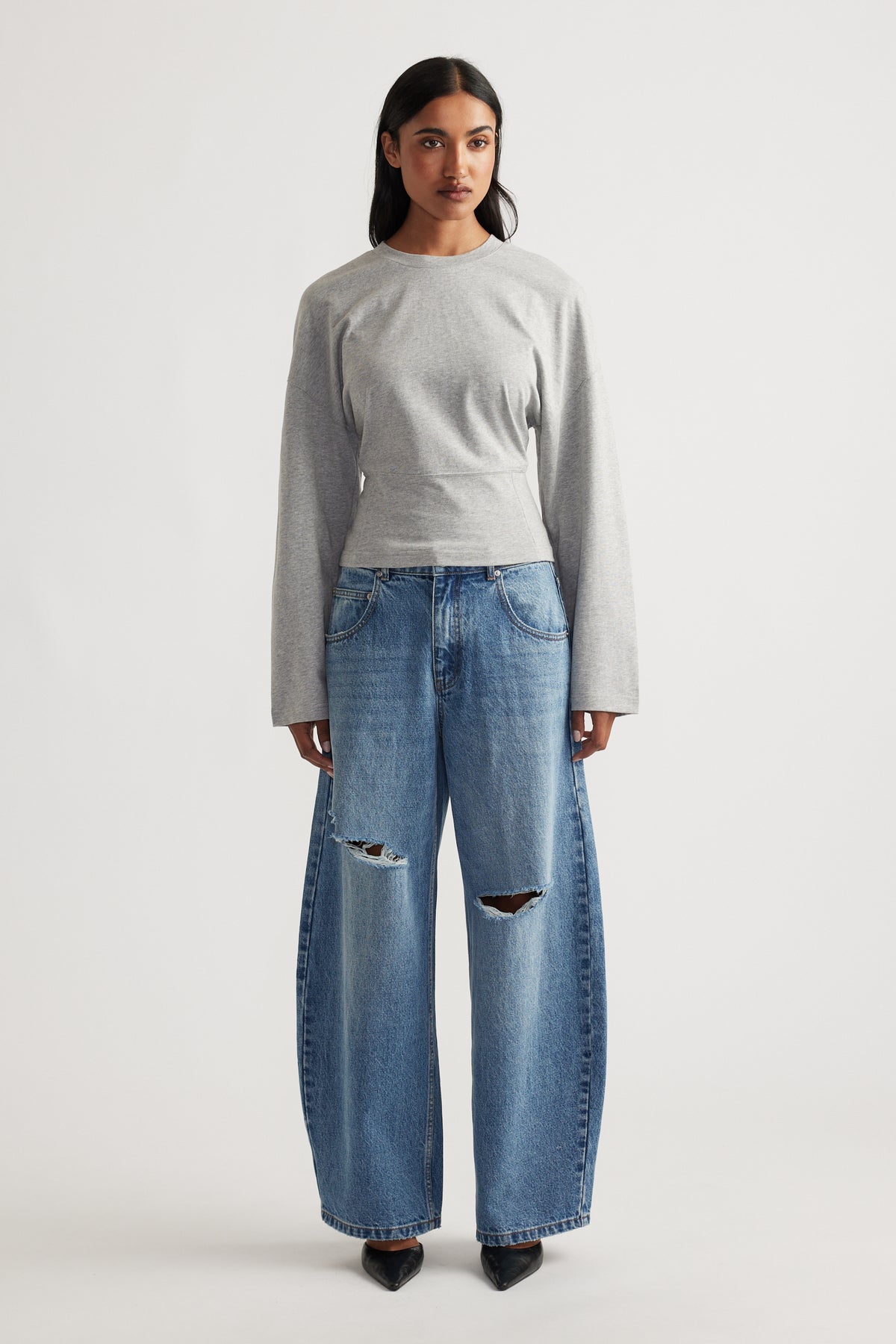 Grey fitted long sleeve top paired with wide-leg distressed blue denim jeans and black pointed shoes