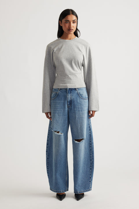 Grey fitted long sleeve top paired with wide-leg distressed blue denim jeans and black pointed shoes