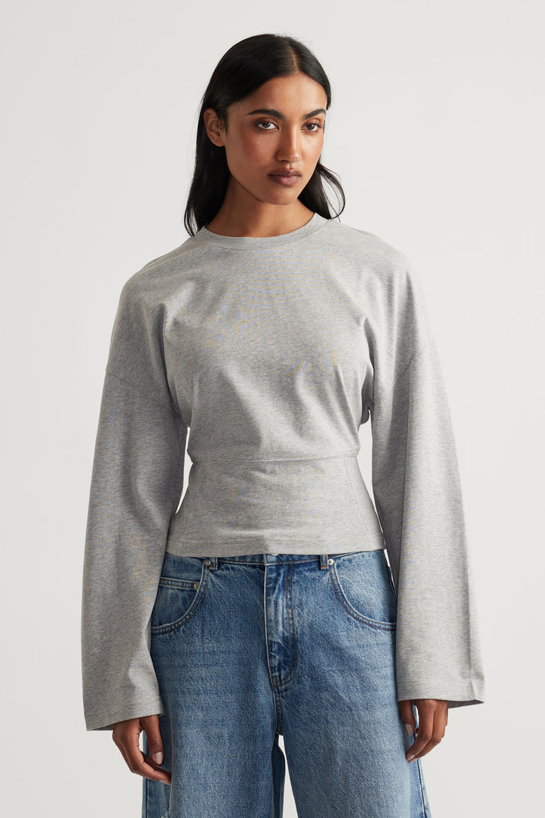 Woman wearing a light grey long sleeve top with wide cuffs paired with relaxed fit blue denim jeans