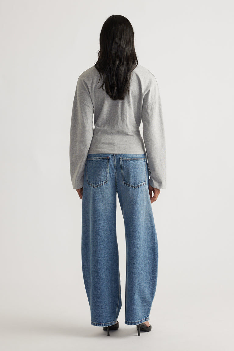 Back view of a soft grey long sleeve top paired with relaxed fit blue denim jeans and black heeled shoes