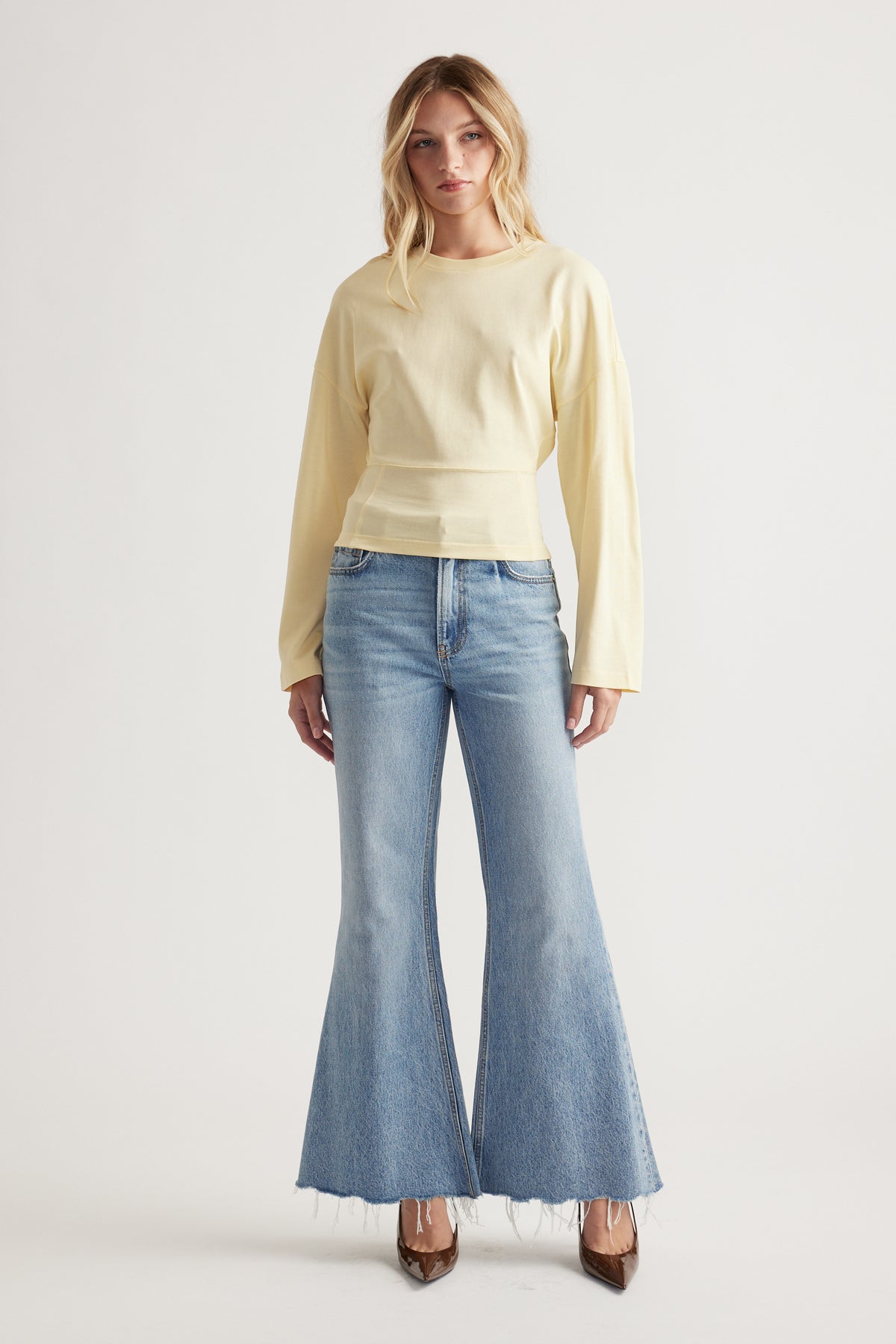 Woman wearing a soft yellow long sleeve top paired with light wash flared jeans and brown pointed shoes