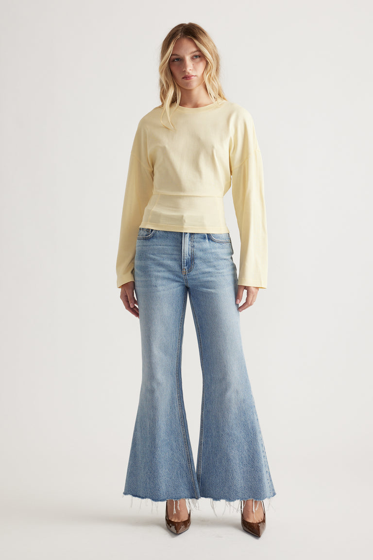 Woman wearing a soft yellow long sleeve top paired with light wash flared jeans and brown pointed shoes