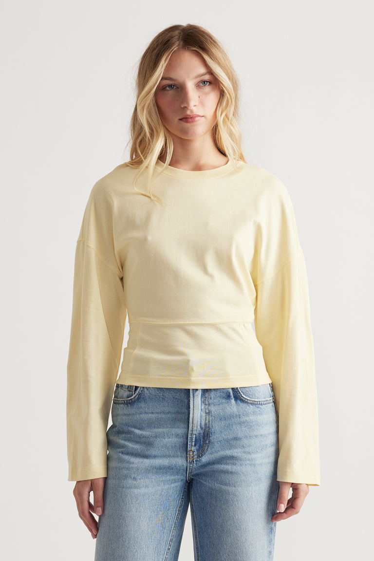 Woman wearing a soft yellow long sleeve top with relaxed shoulders and fitted waist paired with light wash blue jeans