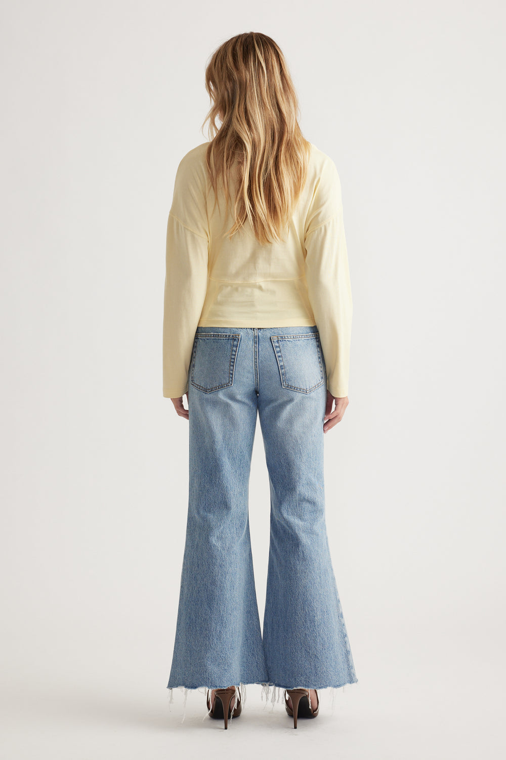Woman with loose blonde hair wearing a pale yellow long sleeve top paired with light wash flared jeans and heels