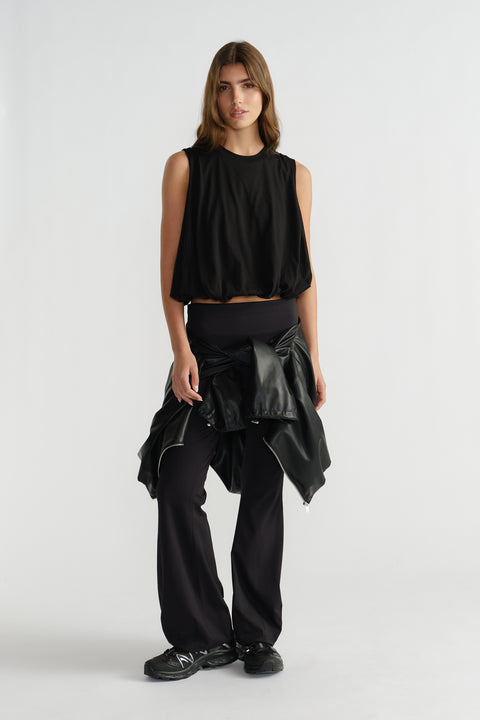 Woman wearing a loose black sleeveless tank with gathered hem, paired with relaxed black pants and a tied jacket at waist