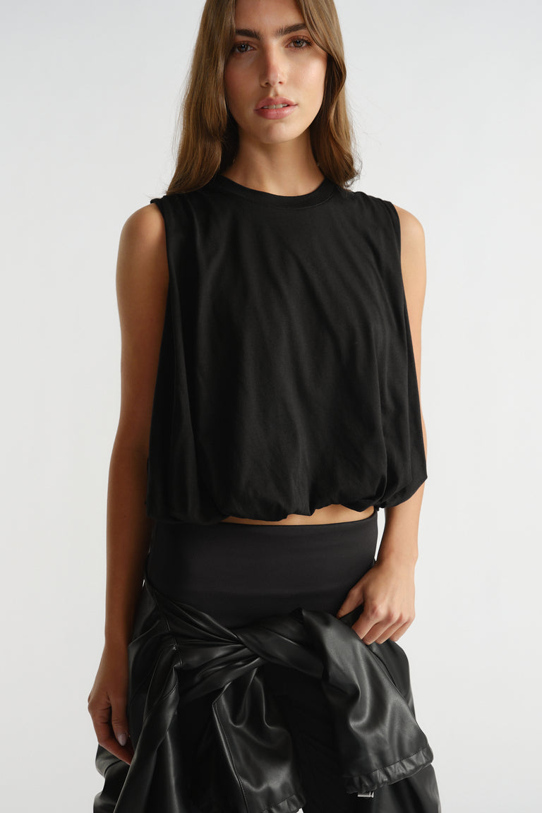 Black sleeveless active tank with a relaxed fit and subtle gathered hem, styled with a tied black jacket at the waist