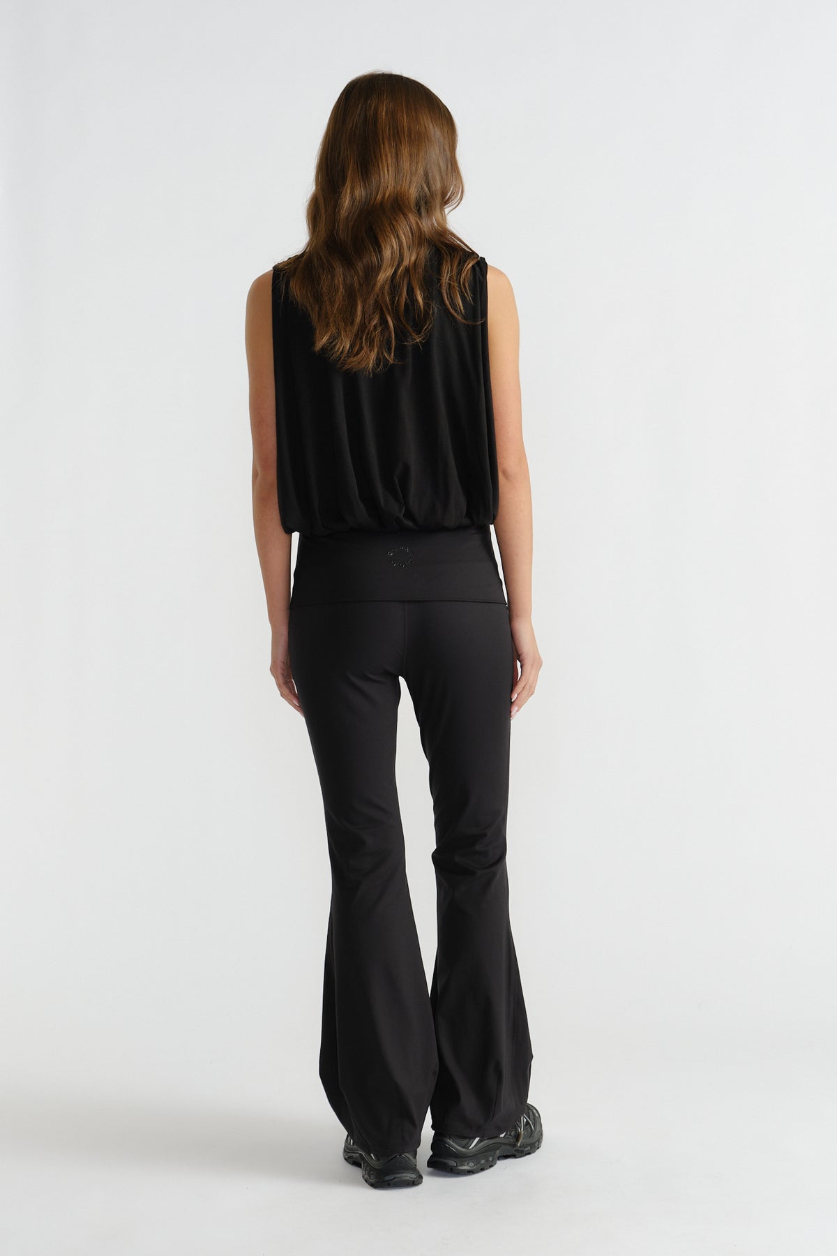Back view of woman wearing a relaxed-fit black sleeveless bubble tank paired with flared black pants and sneakers