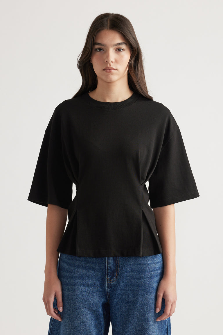 Woman wearing a relaxed black structured tee with wide sleeves paired with casual blue denim jeans against a plain background