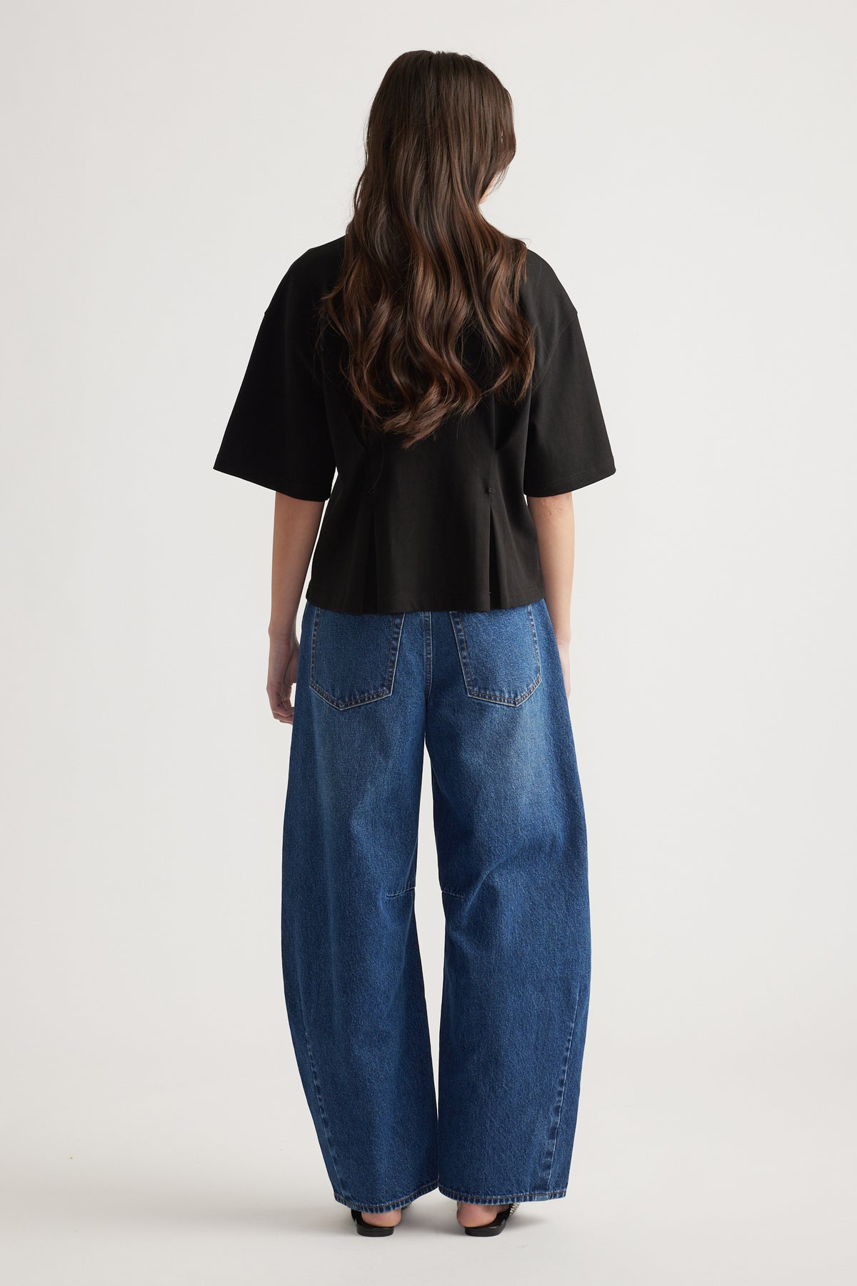 Woman wearing a black structured tee paired with relaxed wide-leg blue denim jeans and black open-toe heels, back view