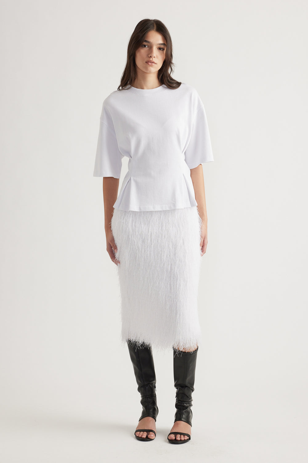 Woman wearing a white structured tee with elbow-length sleeves and a textured midi skirt paired with black heeled boots